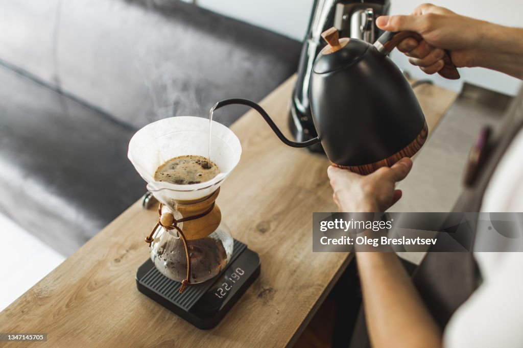 Barista hand pouring water from kettle into filter coffee maker glass coffeemaker