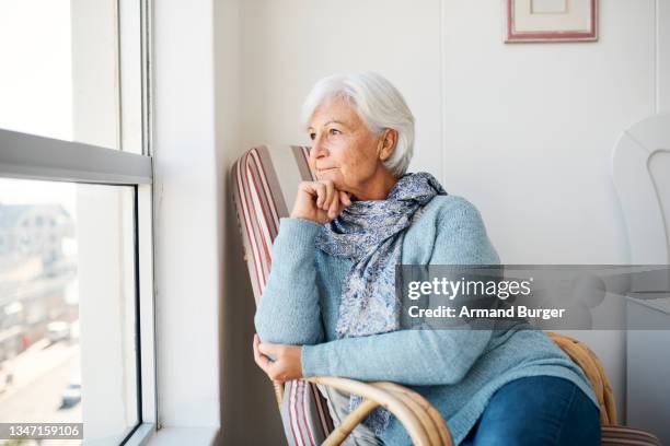 shot of a senior woman looking thoughtfully out of a window at home - 寡婦 個照片及圖片檔