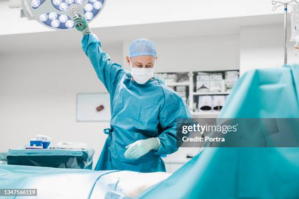 surgeon adjusting surgical light in operating room - operating gown stock pictures, royalty-free photos & images
