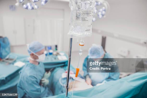 iv drip with surgeons in background at hospital - iv infusion stock pictures, royalty-free photos & images