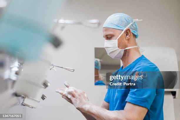 doctor scrubbing fingers near sink in hospital - schoonschrobben stockfoto's en -beelden