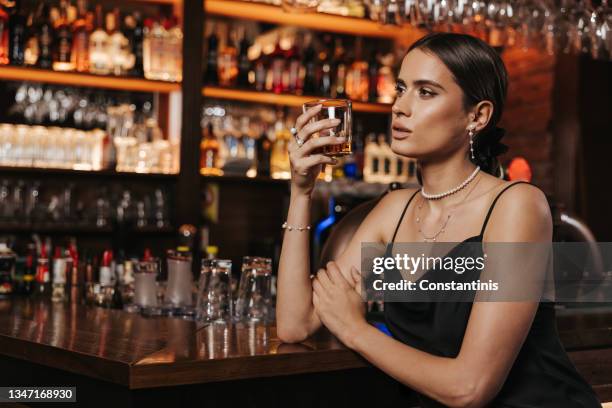 attractive young woman enjoying glass of whiskey in city club - whisky bar stockfoto's en -beelden