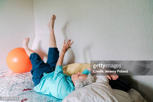 elderly caucasian woman laying on a bed doing her daily exercises with a fitness ball to stay fit, flexible, and strong - 101 stockfoto's en -beelden