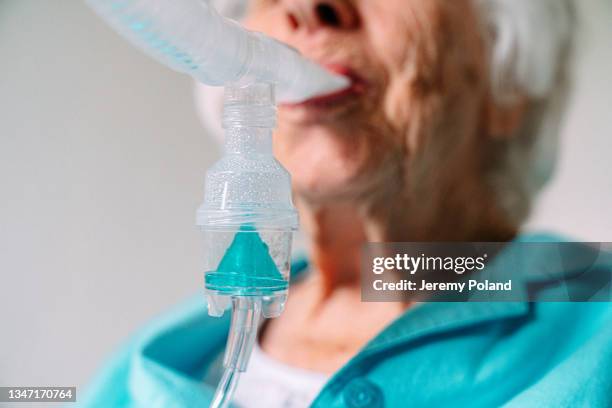 primer plano de ángulo bajo de medicamento líquido azul como una mujer caucásica mayor sentada en casa respirando usando un nebulizador para inhalar medicamentos para tratar el asma o abrir las vías respiratorias pulmonares - compresor de aire fotografías e imágenes de stock