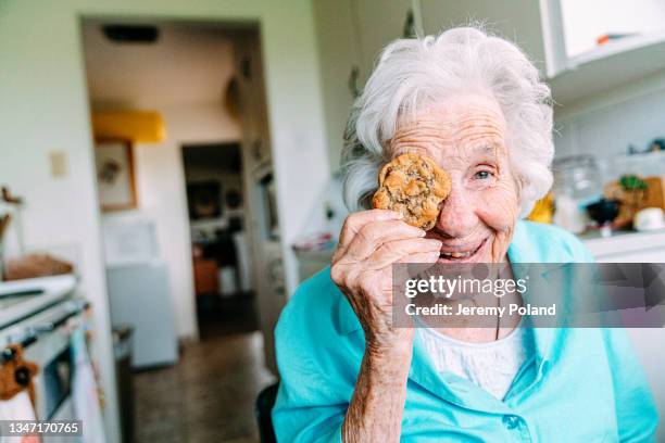 cute portrait of a cheerful, sharp 100-year-old senior woman holding a sweet cookie in front of her eye and smiling at the camera - 109 stock pictures, royalty-free photos & images