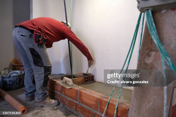 bricklayer worker placing bricks on cement while building the interior walls on a construction site. - pedreiro imagens e fotografias de stock