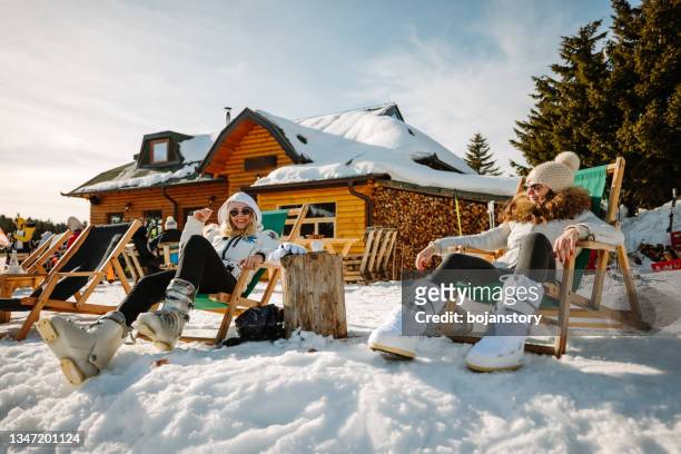 happy female friends relaxing in lounge chairs outdoors - ski resort stock pictures, royalty-free photos & images