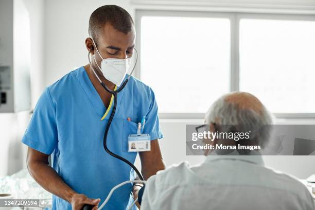 nurse examining patient in clinic during covid-19 - nurse mask - fotografias e filmes do acervo