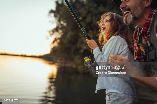 proud grandfather helping out his granddaughter with fishing - fishing imagens e fotografias de stock