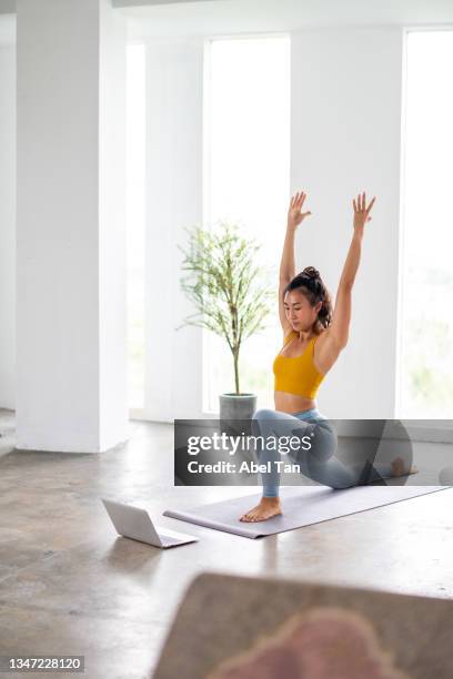 asian female practicing yoga while using laptop stock photo - asian yoga stock pictures, royalty-free photos & images