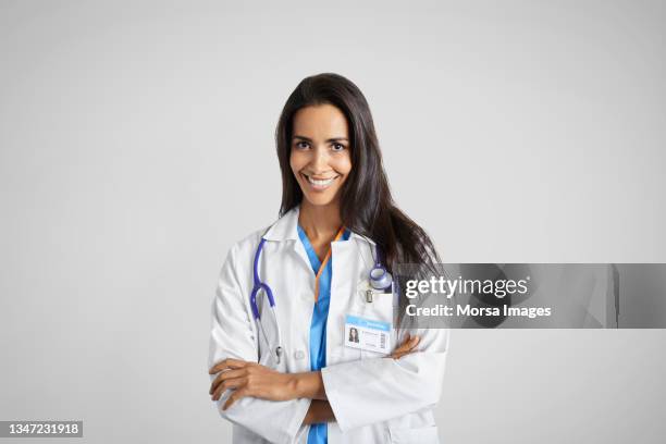 latin american doctor with arms crossed against gray background - doctor with arms crossed stock pictures, royalty-free photos & images
