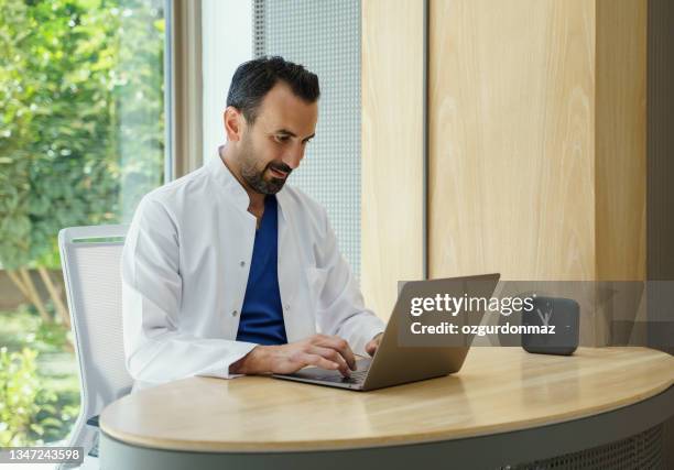 médico do sexo masculino trabalhando em laptop em sua clínica - dental office - fotografias e filmes do acervo