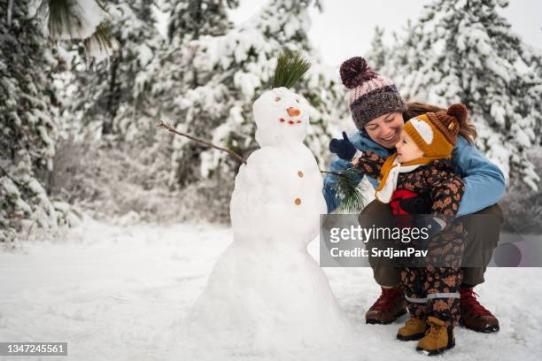 niño pequeño juguetón, ayudando a su madre a hacer un muñeco de nieve - winter family home fotografías e imágenes de stock