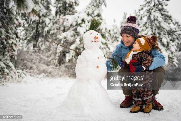 curioso niño toodler observando a su madre mientras ella hace un muñeco de nieve - muñeco de nieve fotografías e imágenes de stock