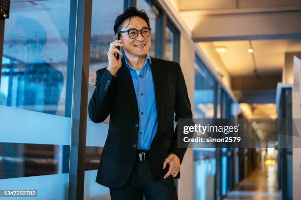 senior businessman talk on mobile phone at modern bright office interior - asian ceo stock pictures, royalty-free photos & images