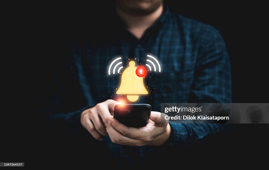 Businessman holding smartphone with virtual yellow bell ringing for application notification alert concept.
