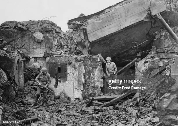 Two American soldiers of the 84th Infantry Division, United States Ninth Army, carrying their M1 semi-automatic carbines, examine the destruction of...