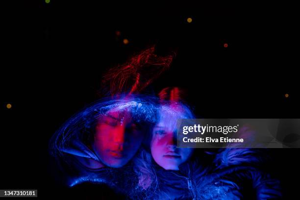 teenage boy and girl, lit by moving red and blue led lights against a dark background at night - couple dark background stock pictures, royalty-free photos & images