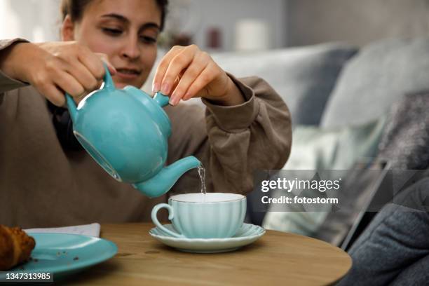 young woman pouring a cup of tea from a teapot - tea bags stock pictures, royalty-free photos & images