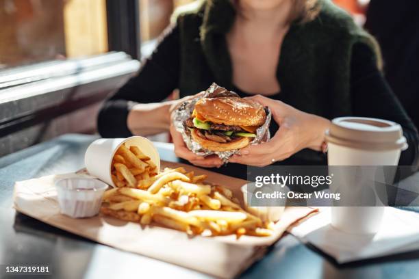 female hands holding s freshly served cheeseburger in an outdoor cafe - 大食い ストックフォトと画像