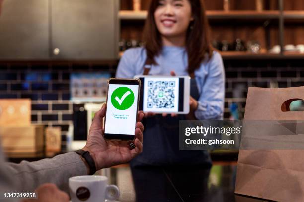 cafe owner accepting mobile payment from customer using smart phone - bar code stockfoto's en -beelden