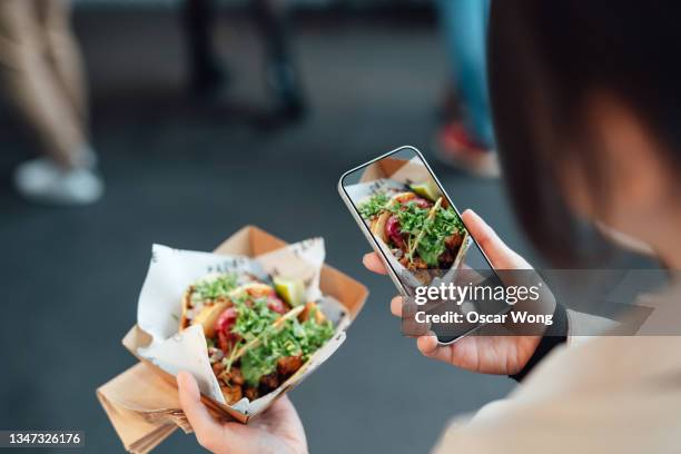 young woman taking picture of her tacos lunch on smart phone in street food market - mexican street market stock pictures, royalty-free photos & images
