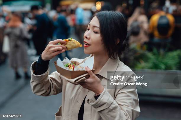 young woman taking lunch break and enjoying tacos in street food market - taco stockfoto's en -beelden