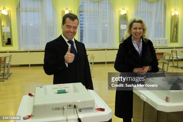 Russian President Dmitry Medvedev gives the thumbs up as he and his wife Svetlana Medvedeva visit a polling station to post their votes during a...