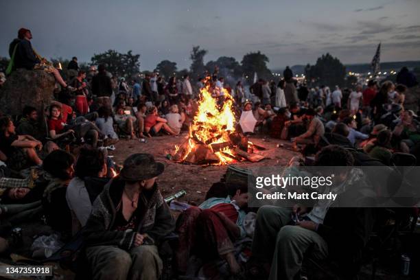 People gather around a camp fire which has been built at the Stone Circle as the sun rises after the final night of the 2011 Glastonbury Festival...