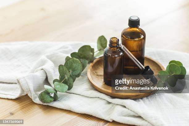 brown amber glass bottle dropper with cosmetic oil with eucalyptus leaves on wooden plate. - essential oils stock pictures, royalty-free photos & images