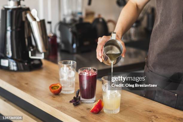 barista's hand pouring organic syrup in glass with fresh iced summer cocktail. sweet natural drink - make stockfoto's en -beelden