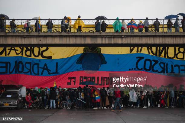 Demonstrators walk and wait for raint to pass below a bridge with a Colombian flag as thousands protested during the marking of the first month of...