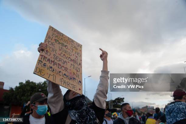 Demonstrator flips the finger to the police helicopter as he carries a sign against police brutality as thousands protest in northern Bogota,...
