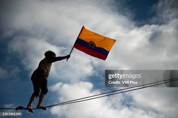 An equilibrist waves a Colombian flag as demonstrator doing as Colombia enters its 4th week of anti-government protests against police brutality that...