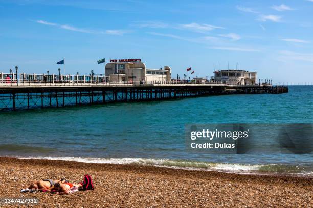 England, West Sussex, Worthing, Worthing Beach, Couple Sunbathing on the Beach with Pier in Background.