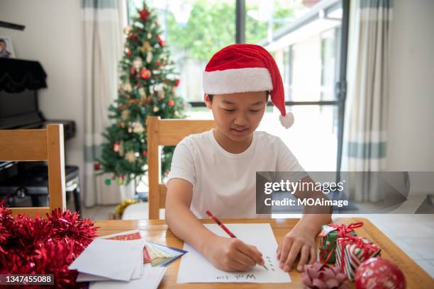 teenage boy is writing a christmas wish list on the table in front of the christmas tree in the living room - writing list stock pictures, royalty-free photos & images