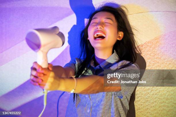 eine modische frau, die einen haartrockner benutzt, um ihre haare im schatten von licht und schatten zu blasen - blow drying hair stock-fotos und bilder