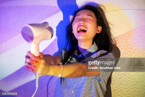 a fashionable woman using a hairdryer to blow her hair under the shadow of light and shadow - blow drying hair stock pictures, royalty-free photos & images