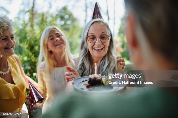 senior woman getting small birthday cake from friends during celebration outdoors on patio at restaurant. - senior birthday stock pictures, royalty-free photos & images