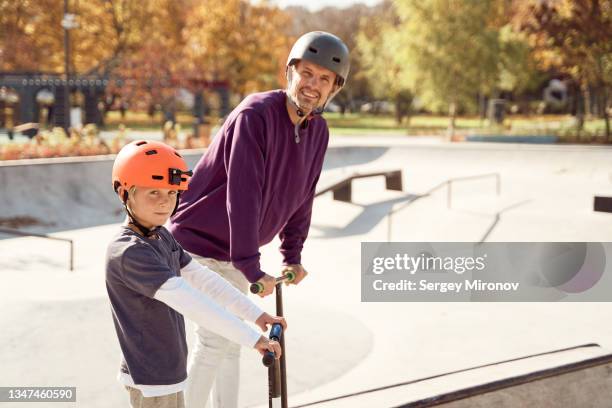 father with son skating on scooter in skate park - roller skates stock-fotos und bilder