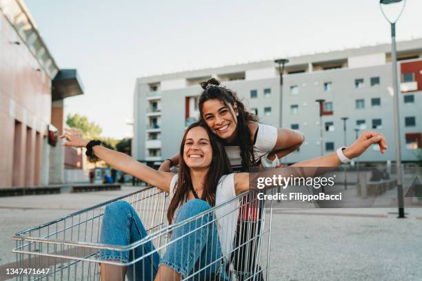 two friends are having fun together with a shopping cart in the city - girl after shopping stock pictures, royalty-free photos & images