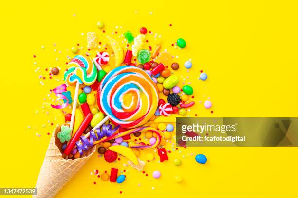 multicolored exploding candies on yellow background - lollipop background stock pictures, royalty-free photos & images