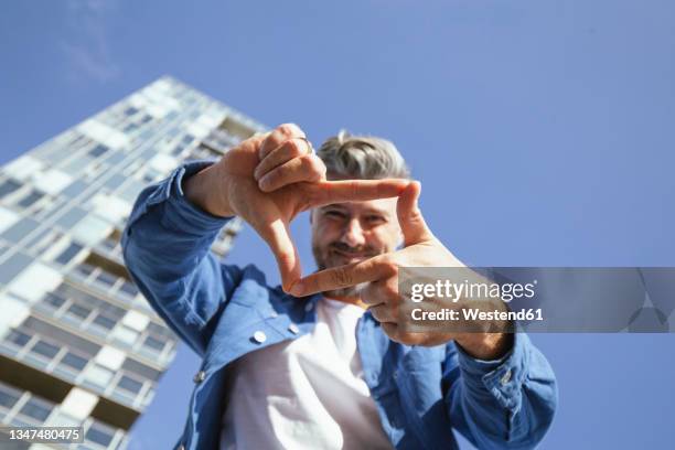 mid adult man making finger frame during sunny day - fingerrahmen stock-fotos und bilder