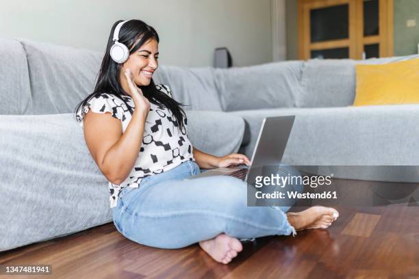 smiling woman waving during video call through laptop in living room - chubby arab stock pictures, royalty-free photos & images