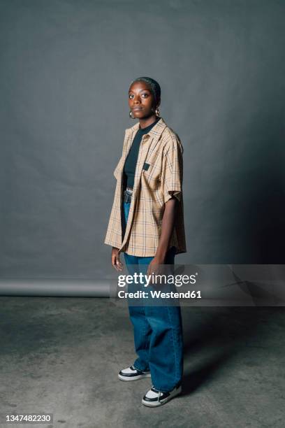 confident young woman standing by gray backdrop in studio - black woman full length stock pictures, royalty-free photos & images