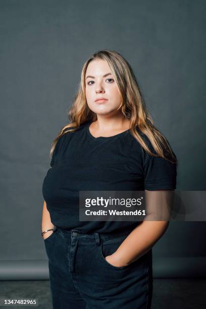 confident voluptuous woman standing with hand in pockets at studio - mannequin grande taille photos et images de collection