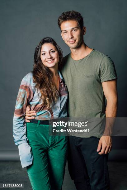 smiling couple standing together against gray backdrop at studio - couple studio stockfoto's en -beelden