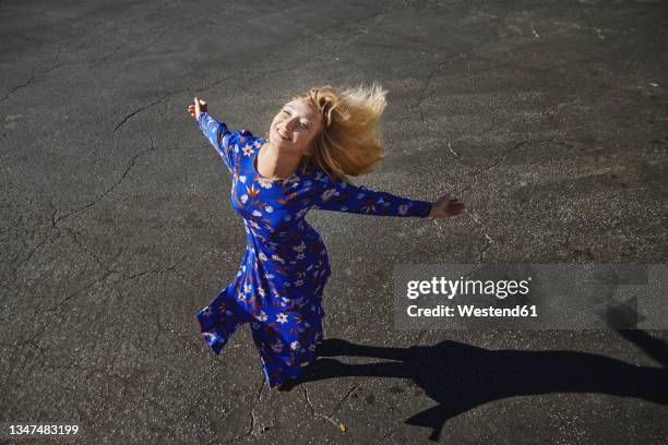 carefree blond woman dancing with arms outstretched on street - 腕を広げる ストックフォトと画像