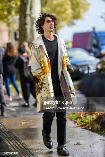 Guest wears a black t-shirt, black suit pants, a beige with yellow / green / black print patten oversized long zipper / hoodie coat, black shiny...