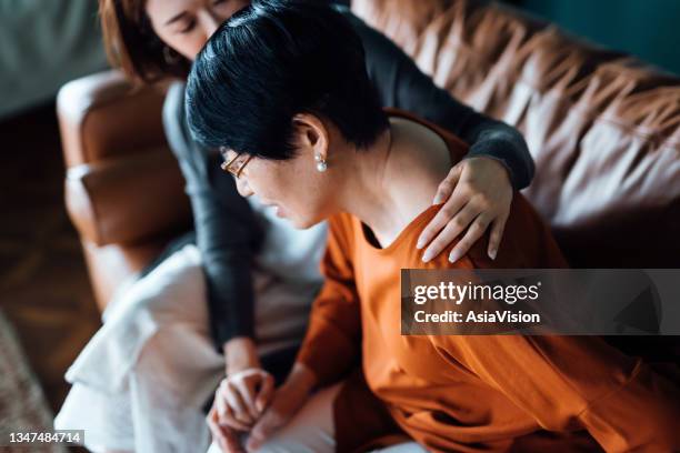 a daughter embraces her elderly mother who is feeling unwell. holding her mother's hand giving support and consoling her while sitting on sofa in the living room at home - woman home with sick children imagens e fotografias de stock